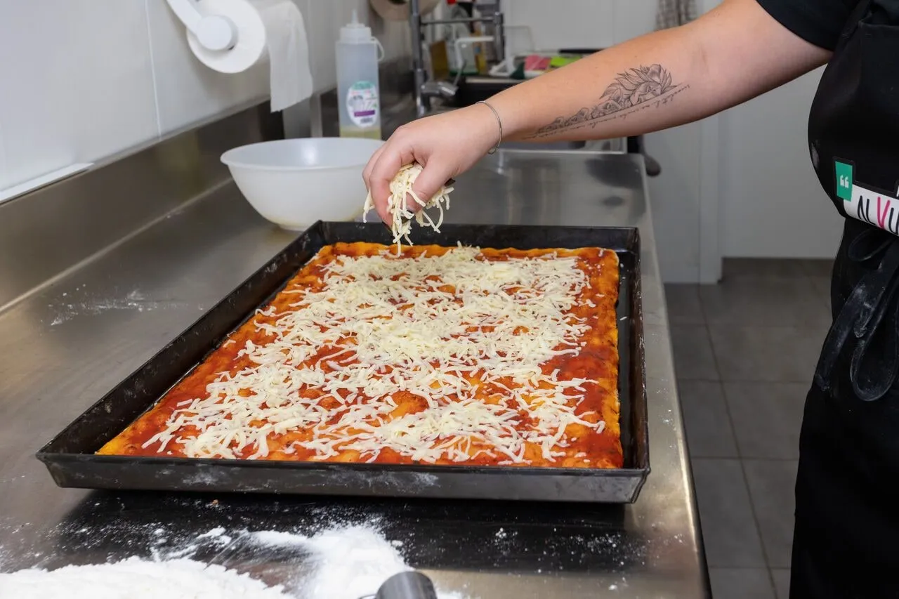Una mano esparce mozzarella rallada sobre la base con tomate.